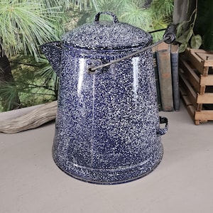 May include: A vintage blue and white enamel camping coffee pot with a wire handle and a lid. The pot has a speckled white finish on a dark blue background.