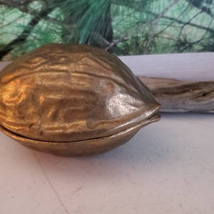 May include: A brass nutcracker shaped like a walnut. The nutcracker is closed and has a detailed, textured surface.
