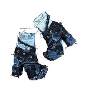 May include: Two denim boots made from patchwork denim pieces. Each boot features a light blue tag with text and a logo. The boots have a distressed, deconstructed aesthetic with visible stitching and metal eyelets.