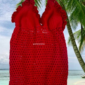 May include: Red crocheted halter top with a ruffled neckline and a mesh design. The top is photographed against a tropical background.
