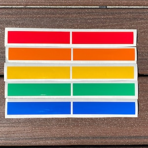 May include: Five rectangular stickers with white borders, arranged vertically. The stickers are red, orange, yellow, green, and blue.
