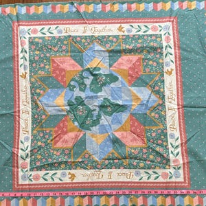 May include: A green fabric with a white and pink patchwork design. The fabric has a repeating pattern of a star with the words "Peace If Together" in a circle around it.