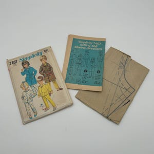 May include: Three vintage Simplicity sewing pattern packets. The main pattern packet features illustrations of children in various outfits. The other packet is a cutting and sewing directions booklet. A brown paper pattern piece is also included.