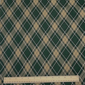 May include: Green and tan plaid fabric with a diamond pattern. The fabric has a woven texture and a ruler is placed at the bottom of the image, showing inch measurements.