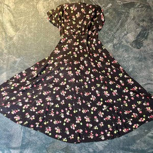 May include: A black floral dress with a V-neckline and short sleeves. The dress has a fitted bodice and a flowing skirt with a small floral print.