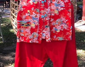 Pode incluir: Um conjunto de pijama de seda vermelho com estampa floral e botões azuis. A parte superior tem gola mandarim e mangas curtas. As calças são largas e têm perna larga.