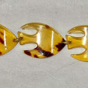 May include: A gold-toned bracelet featuring five fish-shaped links. Each link has a glossy, tortoiseshell pattern with shades of brown and yellow. The bracelet is connected with small gold-colored rings and a clasp.