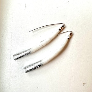 May include: A pair of handmade earrings featuring a white, curved design with silver-colored ends. The earrings have a simple, elegant style with silver-tone ear wires and small decorative accents near the top.