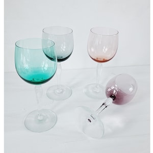 May include: Four wine glasses with different colored glass. The glasses are clear, green, pink, and purple.