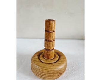 May include: A wooden candle holder with a cylindrical base and a tall, fluted column. The holder is made of light brown wood and has a natural finish.