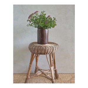 May include: A brown ceramic vase with a bouquet of pink flowers sits on a round wicker stool with four legs.