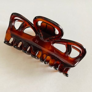 May include: A brown plastic hair claw with a unique, intricate design. The claw has a series of teeth on the bottom for holding hair.