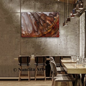 A painting of a guitar with a red, orange, and gold color scheme. The guitar is hanging on a concrete wall in a restaurant setting. The painting is titled 'Nandita Arts'.