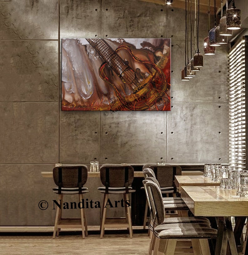 A painting of a guitar with a red, orange, and gold color scheme. The guitar is hanging on a concrete wall in a restaurant setting. The painting is titled 'Nandita Arts'.