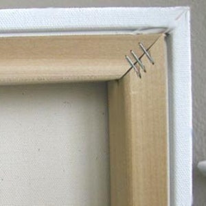 May include: Close-up of a corner of a stretched canvas, showing the wooden frame and staples securing the canvas to the frame.