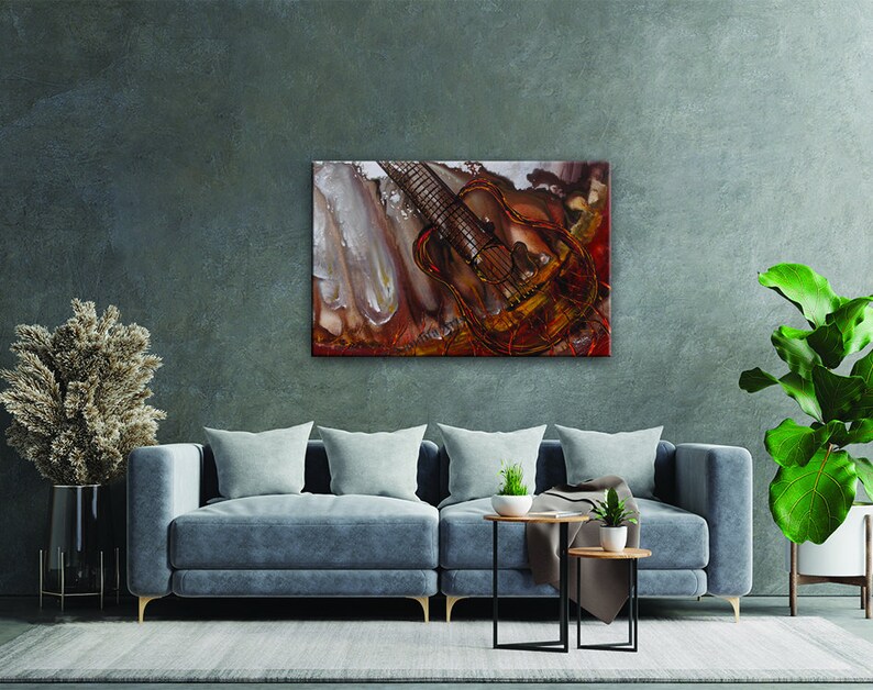 A painting of a guitar with a red, orange, and yellow background. The guitar is painted in a realistic style and has a brown body and a black neck. The painting is framed and hanging on a wall in a living room.