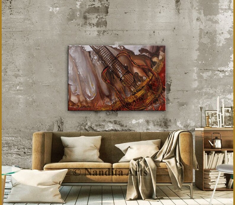 Abstract painting of a brown acoustic guitar with red and gold accents on a textured background. The painting is displayed on a wall above a brown couch with throw pillows and a blanket.