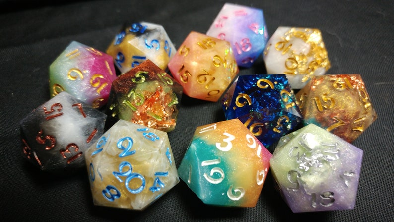 May include: A set of ten iridescent dice with gold and white numbers. The dice are made of resin and have a variety of colors, including pink, blue, green, and orange.