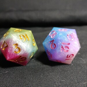 May include: Two iridescent dice with gold numbers. The dice are a gradient of pink, blue, and green.
