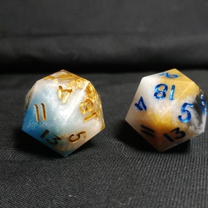 May include: Two white, blue, and gold dice with black numbers. The dice are made of resin and have a cloudy, marbled appearance.