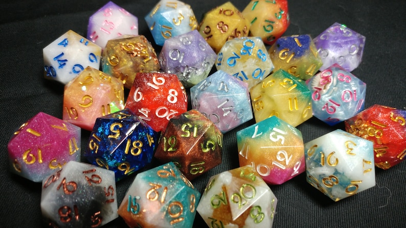 May include: A collection of 20-sided dice with various colors and glitter embedded in the resin. The dice are numbered 1 through 20 with gold lettering.