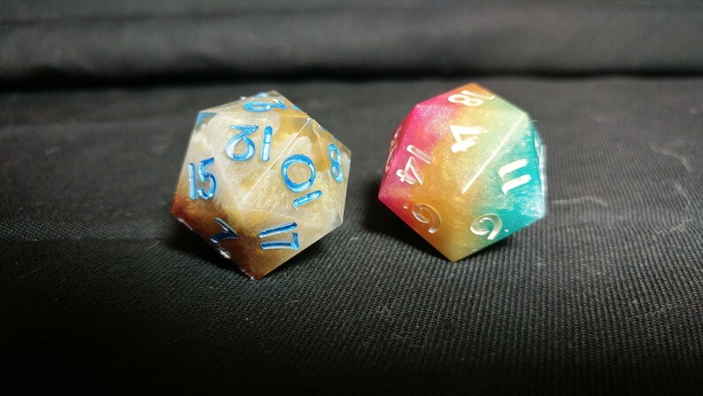 May include: Two multi-colored dice with white numbers. One die is brown and white with blue numbers, the other is a rainbow color with white numbers.