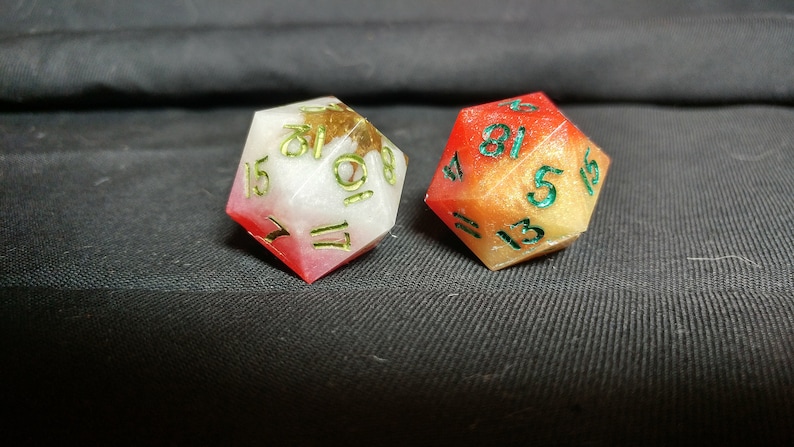 Pu&ograve; includere: Due dadi multicolori con numeri verdi. Un dado &egrave; rosso e bianco con macchie dorate, l'altro &egrave; arancione e giallo con macchie dorate.