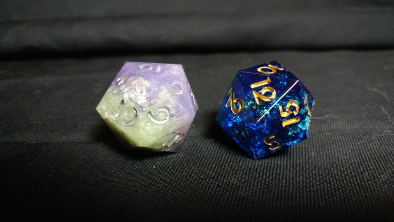 May include: Two iridescent dice, one purple and green with silver numbers, the other blue with gold numbers.