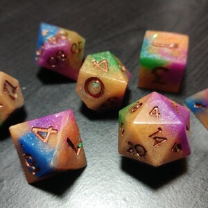 Puede incluir: Un juego de siete dados poli&eacute;dricos con un aspecto colorido y veteado. Los dados presentan una mezcla de colores que incluyen azul, morado, verde y dorado. Los n&uacute;meros son de color cobre. Ideales para juegos de mesa.