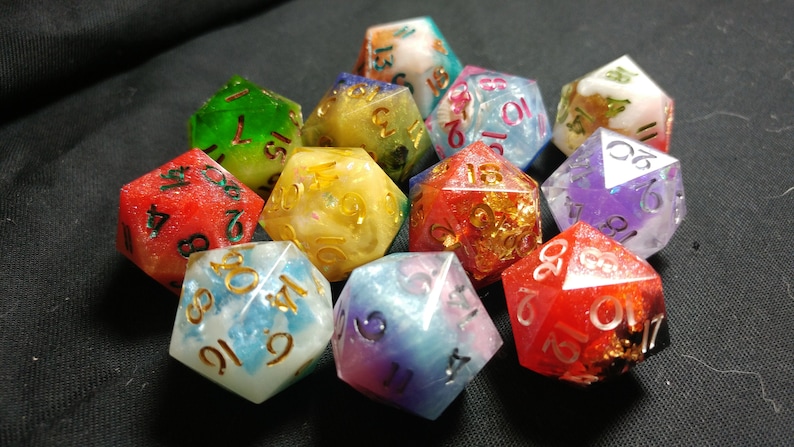 Pu&ograve; includere: Un set di dieci dadi multicolori con glitter dorati e argentati incorporati nella resina. I dadi sono numerati da 1 a 6 e presentano una variet&agrave; di colori, tra cui rosso, verde, blu, viola e giallo.