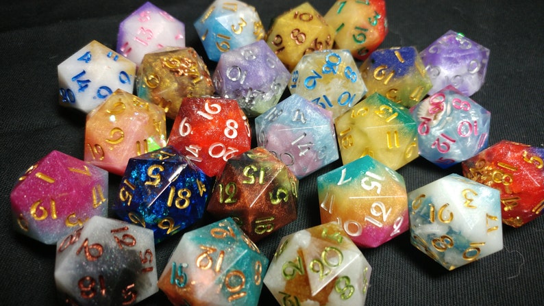 Pu&ograve; includere: Una collezione di dadi a 20 facce con vari colori e glitter incorporati nella resina. I dadi sono numerati da 1 a 20 con lettere dorate.