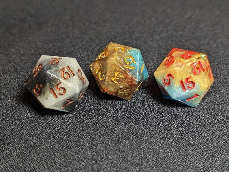 May include: Three multi-colored dice with gold, black, and blue swirls. The dice have numbers 1 through 6 on each side.