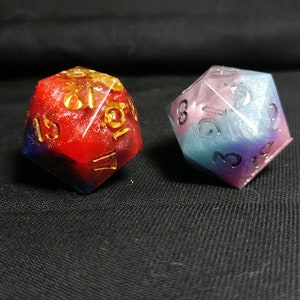 Pu&ograve; includere: Due dadi multi-colorati e iridescenti in resina con numeri dorati. Il dado a sinistra &egrave; rosso e blu, mentre quello a destra &egrave; blu, rosa e viola.