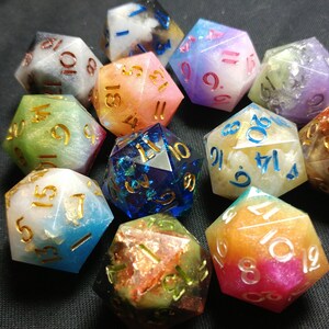 May include: A set of 12 iridescent dice with gold numbers. The dice are made of resin and have a variety of colors, including blue, green, pink, and purple. Each die has a different color and pattern.