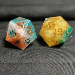 Pu&ograve; includere: Due dadi multicolori con numeri dorati. I dadi sono in resina e hanno una finitura scintillante. Un dado &egrave; turchese, bianco e rame, e l'altro &egrave; giallo, bianco e verde.