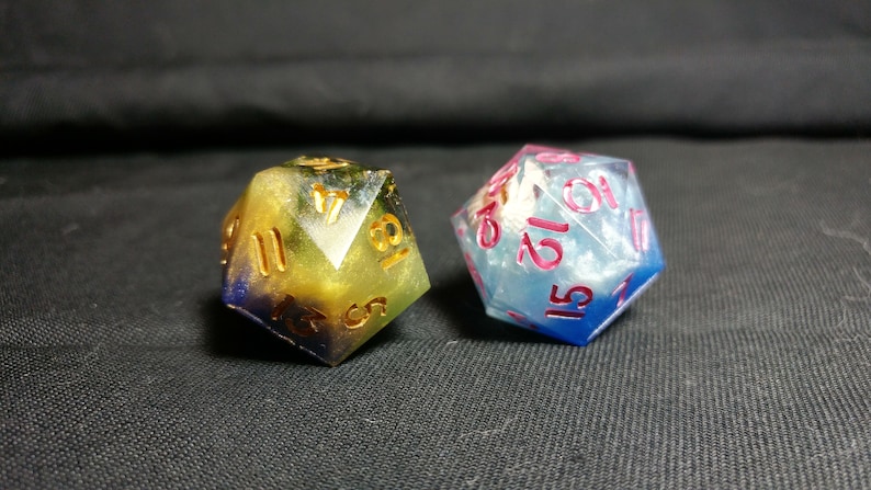 Pu&ograve; includere: Due dadi iridescenti con numeri dorati e rosa. I dadi sono multicolori con vortici blu, verdi e gialli. Un dado &egrave; blu e bianco con una finitura scintillante.