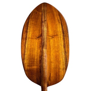 May include: A wooden paddle with a rounded, oval-shaped blade. The blade is made of a rich, dark brown wood with a natural grain pattern. The paddle is designed for paddling in water.