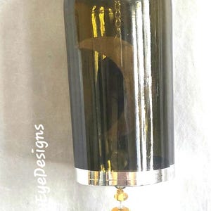 May include: A repurposed wine bottle wind chime. The dark green bottle has a silver rim and a decorative hummingbird charm. The charm is suspended by a chain of beads and a gold-colored metal hook.