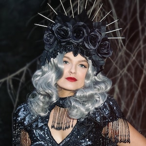 May include: A woman wearing a black sequined dress with fringe detailing and a black crown of roses. She has silver hair and is wearing black gloves.