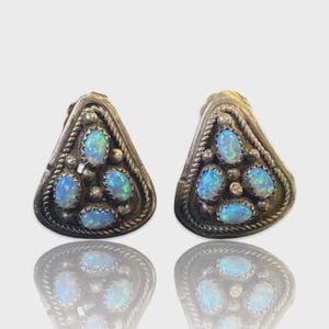 May include: A pair of silver-toned triangular earrings. Each earring features five oval-shaped, opalescent blue gemstones. The edges are adorned with a twisted rope design, and small silver beads are interspersed around the gemstones.