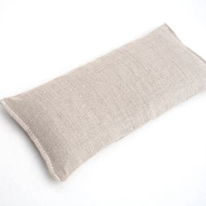 May include: A beige linen eye pillow. The pillow is rectangular and has a seam down the center.