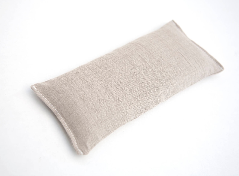 May include: A beige linen eye pillow. The pillow is rectangular and has a seam down the center.