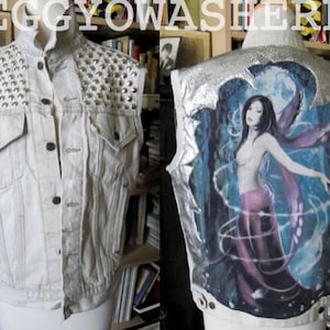 May include: A light-colored denim vest with silver studs on the shoulders. The back of the vest features a fantasy art print of a woman with purple wings and a moonlit forest scene. The vest has a button-up front.