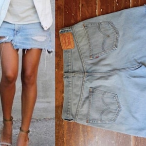 May include: Light blue denim skirt with distressed details, featuring a raw hem. The skirt has a classic five-pocket design and a leather patch with a red logo. The skirt is shown on a person and also laid flat on a wooden surface.