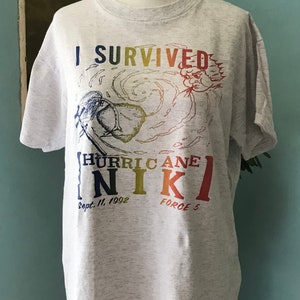 May include: A grey t-shirt with a colorful graphic that says "I Survived Hurricane Niki Sept. 11, 1992 Force 5".