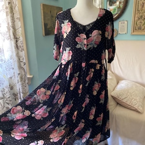 May include: Black floral dress with pink roses and white polka dots. The dress features a scoop neckline with lace trim, short sleeves, and a button-down front. The skirt is flowing and gathered at the waist.