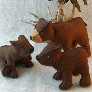 May include: Three brown felt bears, one standing and two sitting, with a green felt tree in the background.