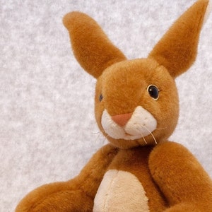 May include: A brown plush bunny rabbit with white fur on its nose and chest. The bunny has black eyes and a long, fluffy tail.