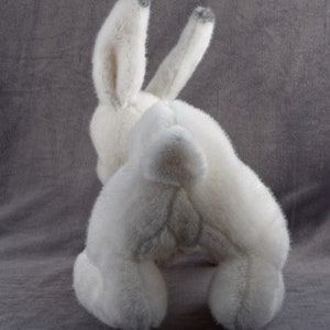 May include: White plush bunny rabbit toy with gray fur on the ears. The bunny is sitting on a gray surface.
