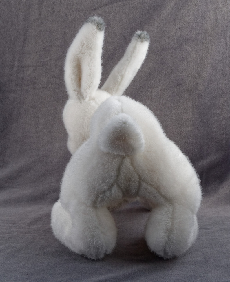 May include: White plush bunny rabbit toy with gray fur on the ears. The bunny is sitting on a gray surface.